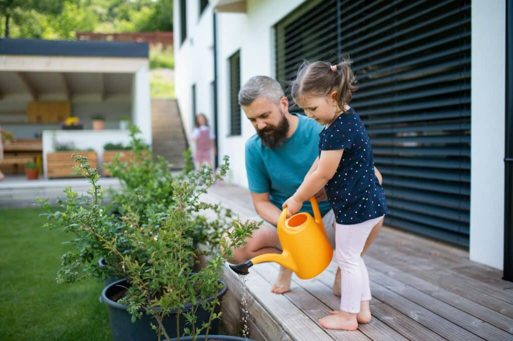 Landscaping maintenance Father and daughter outdoors in the backyard, watering plants